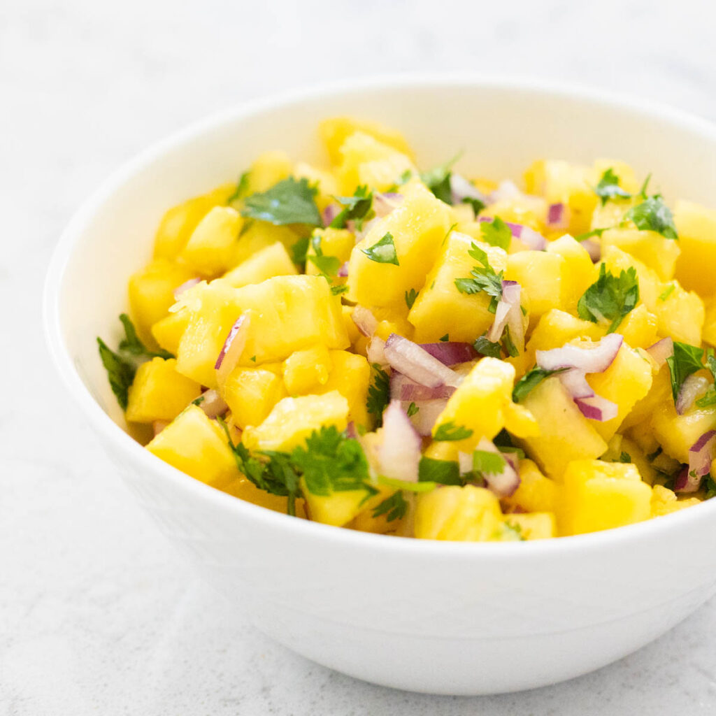 The white bowl filled with pineapple salsa.