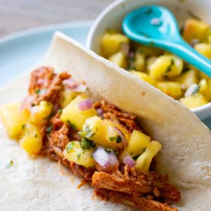 A serving of pineapple salsa has been spooned over a shredded chicken taco.