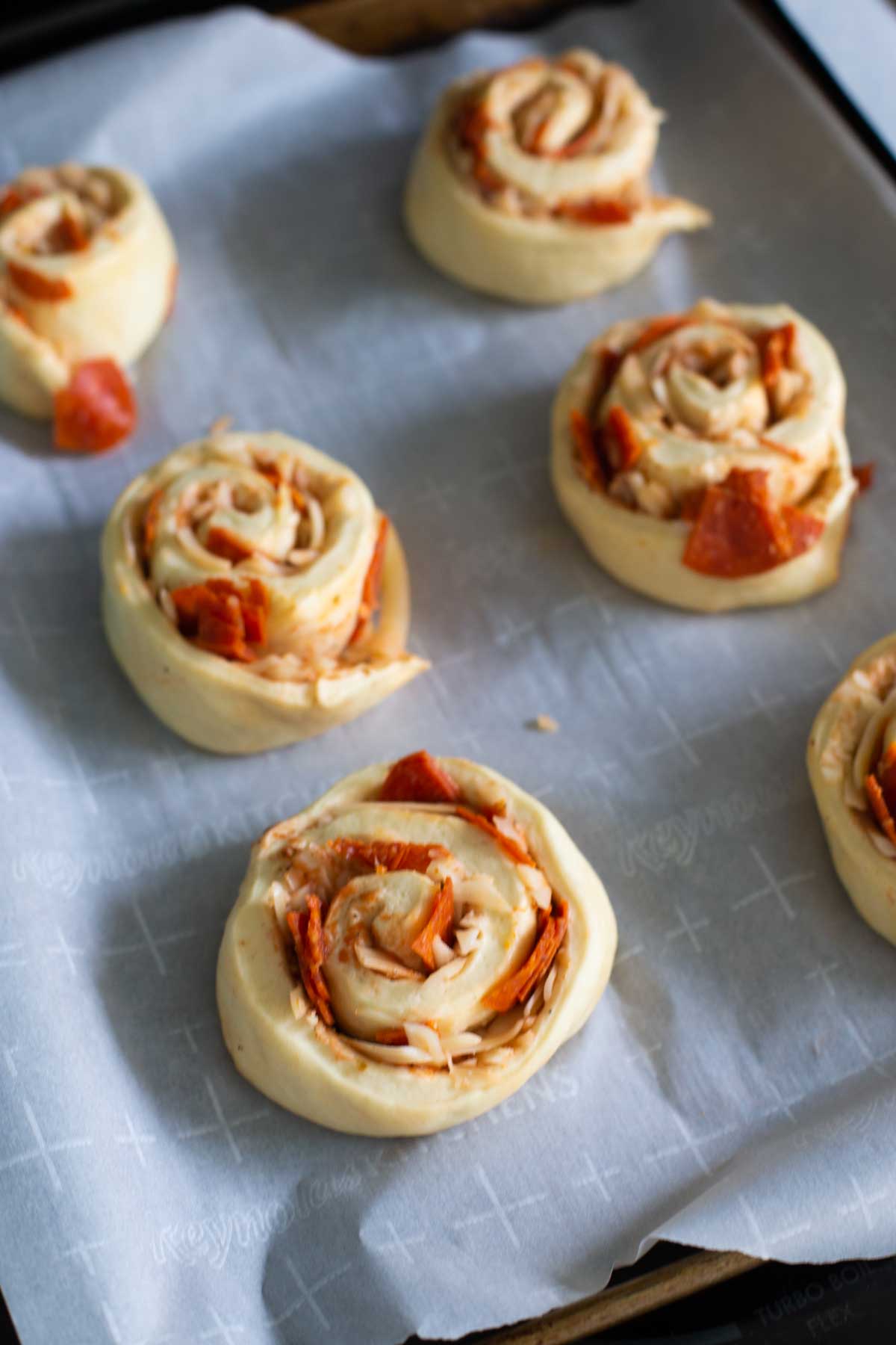 The pizza buns have been placed on a parchment lined baking sheet to rise.