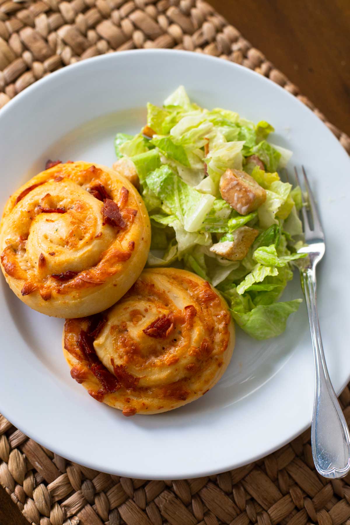 The pizza buns are on a plate next to a green salad with croutons.