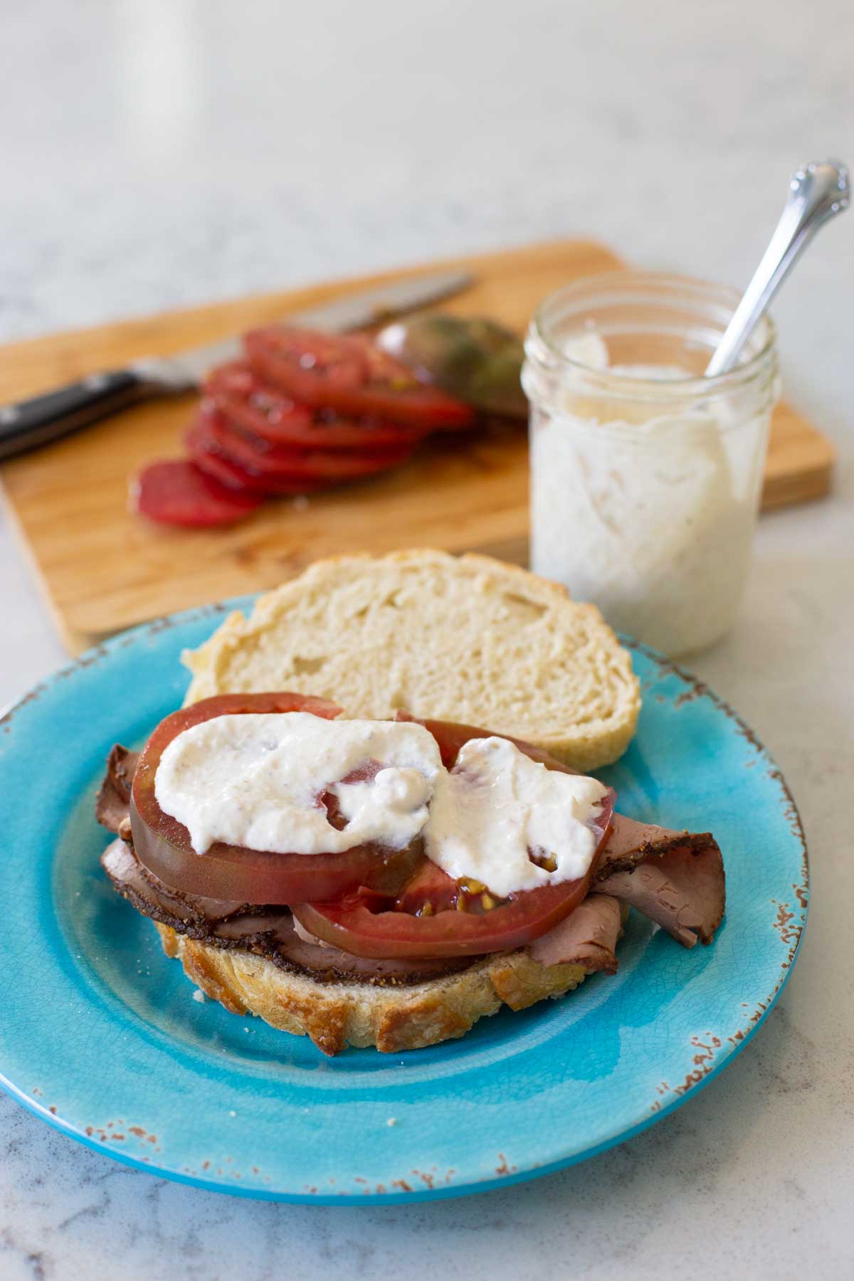 A sour cream horseradish sauce is spread over a roast beef sandwich with sliced tomatoes.