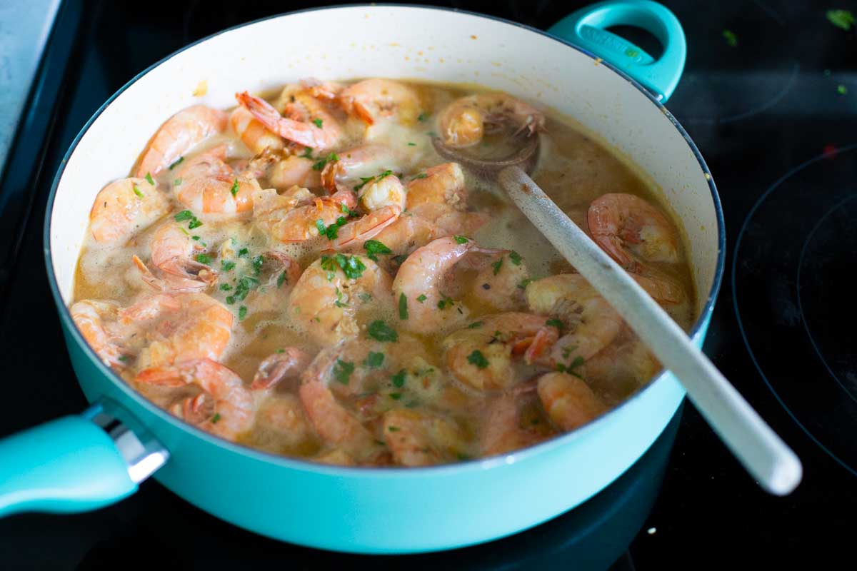 The shrimp are being cooked in a large skillet with butter wine sauce.