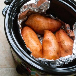 A slow cooker pot has several sweet potatoes in it ready to bake.