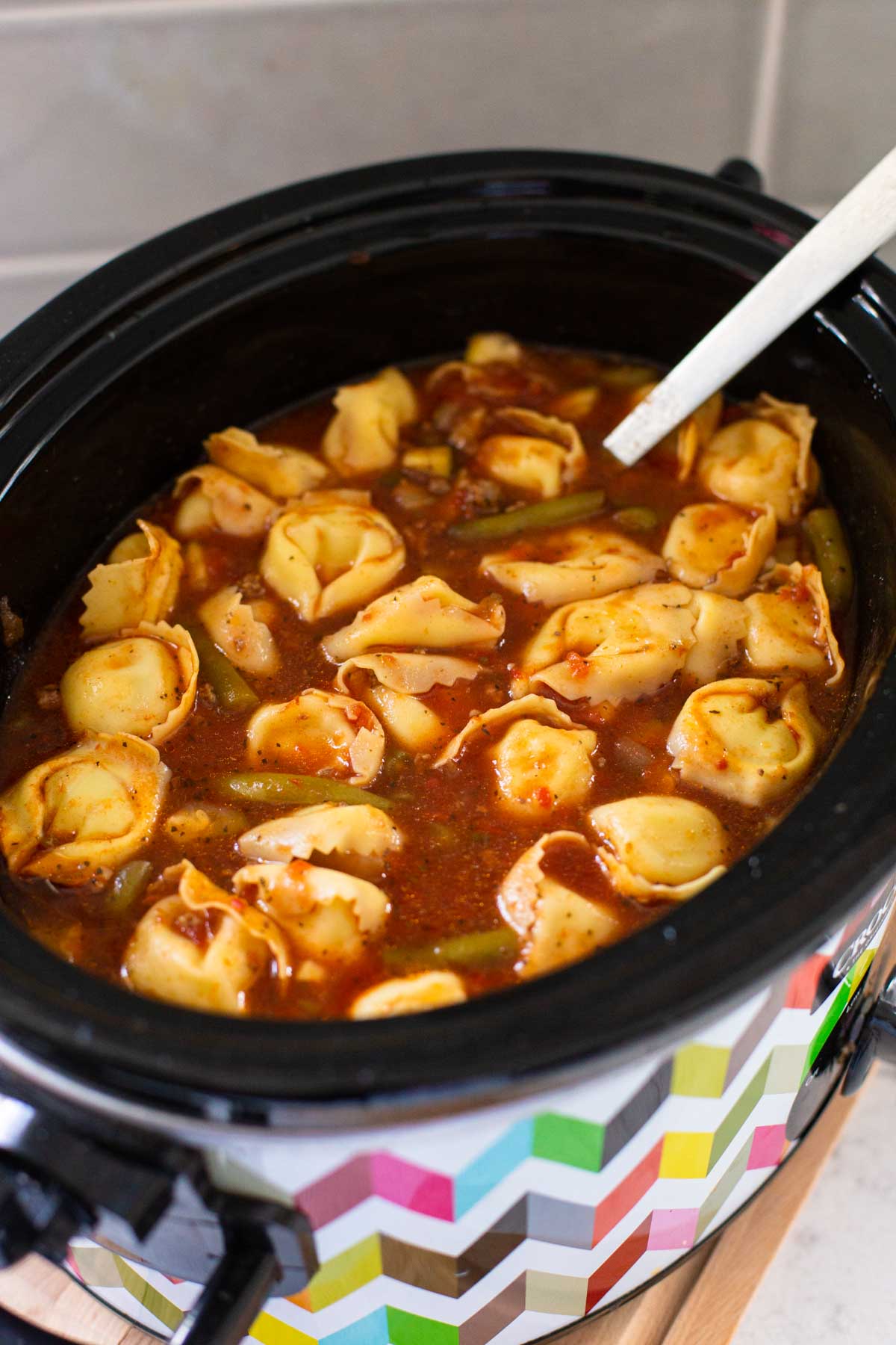 A crockpot has the tortellini soup ready to be served.