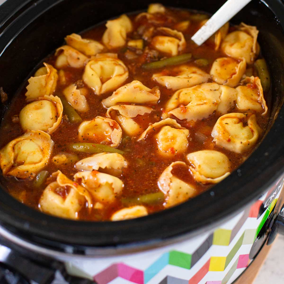 A crockpot has tortellini soup with a tomato broth base.