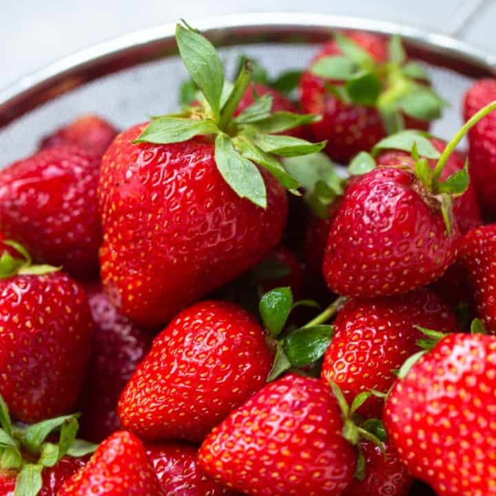 A collander filled with fresh strawberries about to be rinsed.