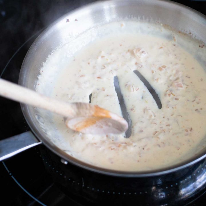 A white cream sauce in a skillet is being prepared for a white pizza base.