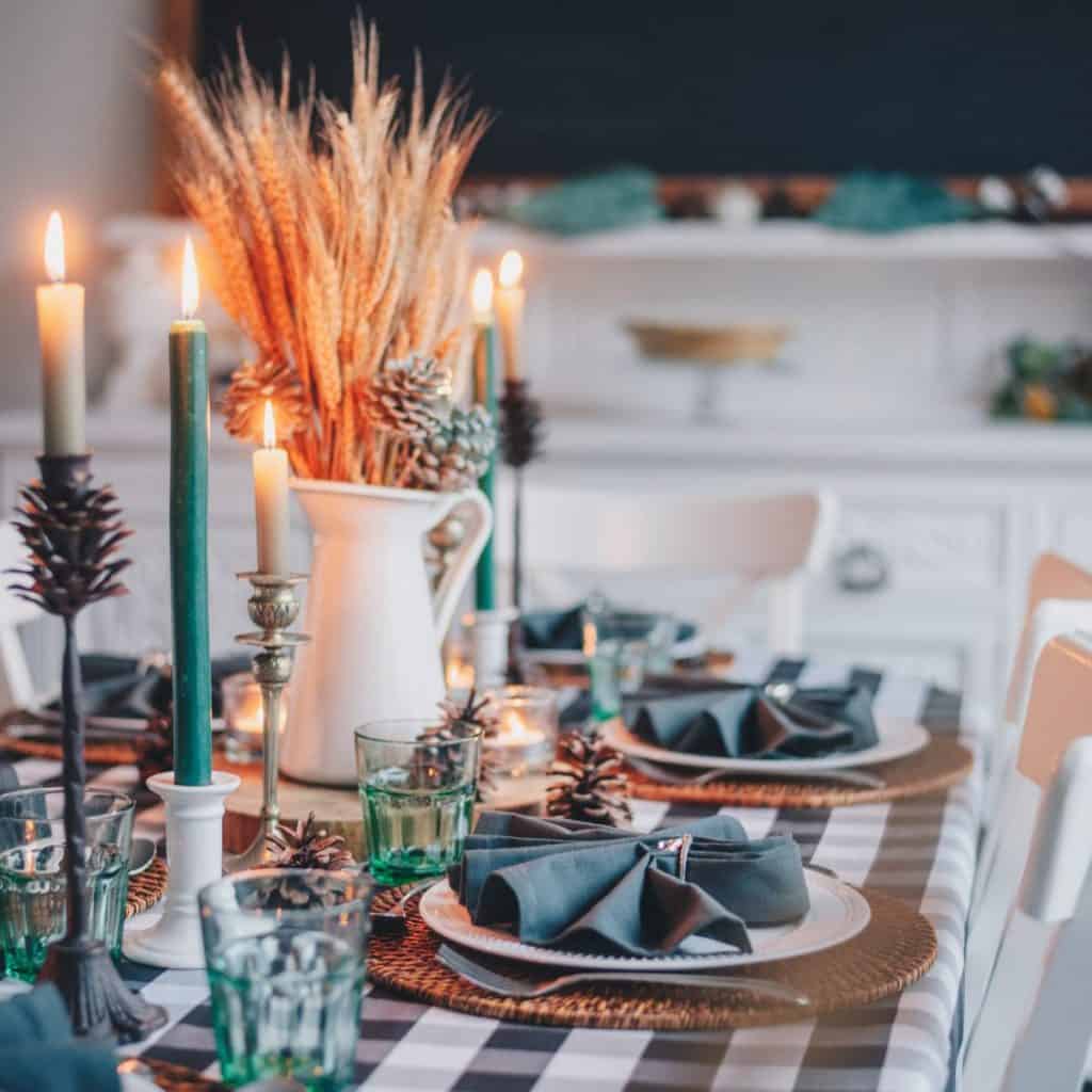 The family dinner table is set for a special meal with pretty napkins, candles, and a vase filled with wheat.