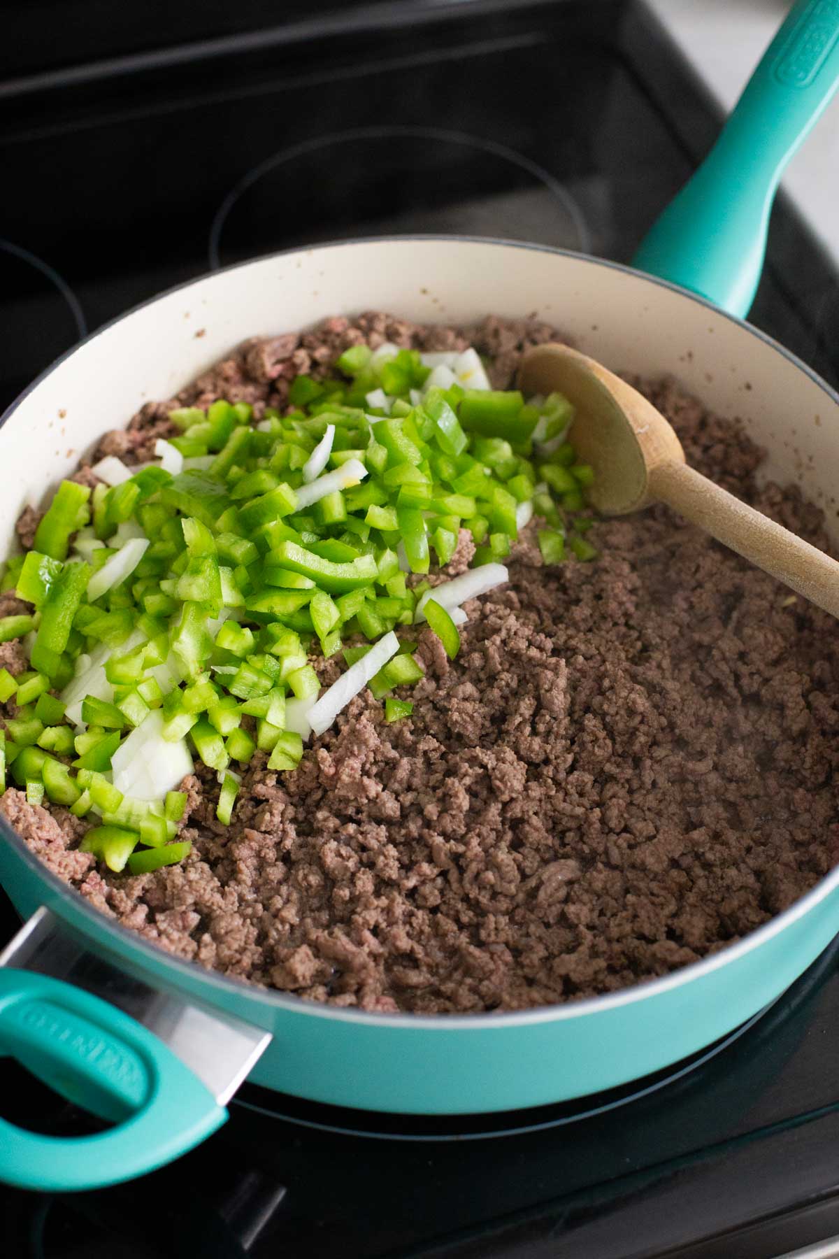 The ground beef and green peppers have been added to a large skillet to be cooked.