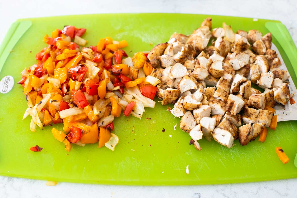 The chicken and peppers have been diced into smaller pieces on a cutting board.