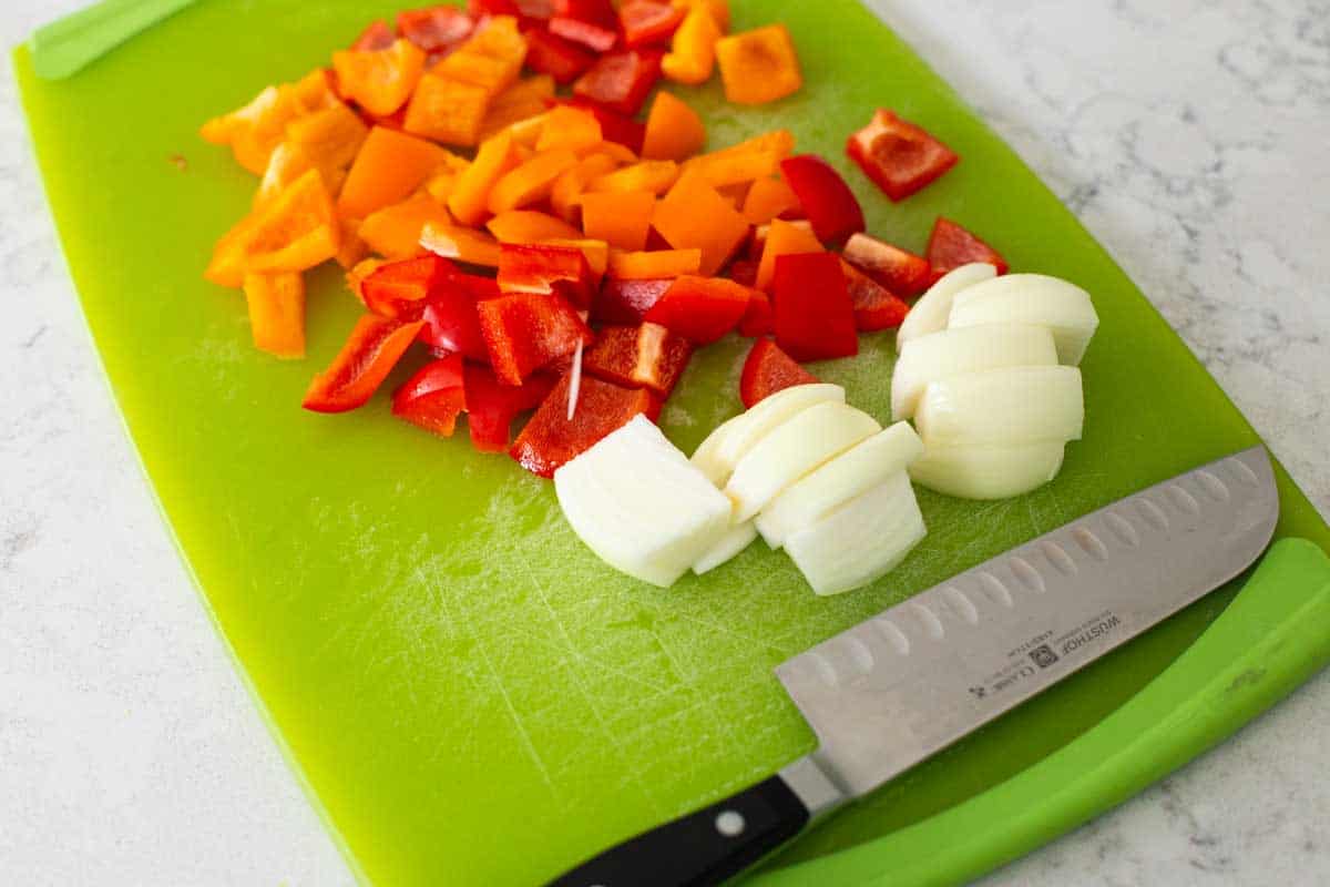 A cutting board has chopped red and yellow bell peppers and a chopped onion.