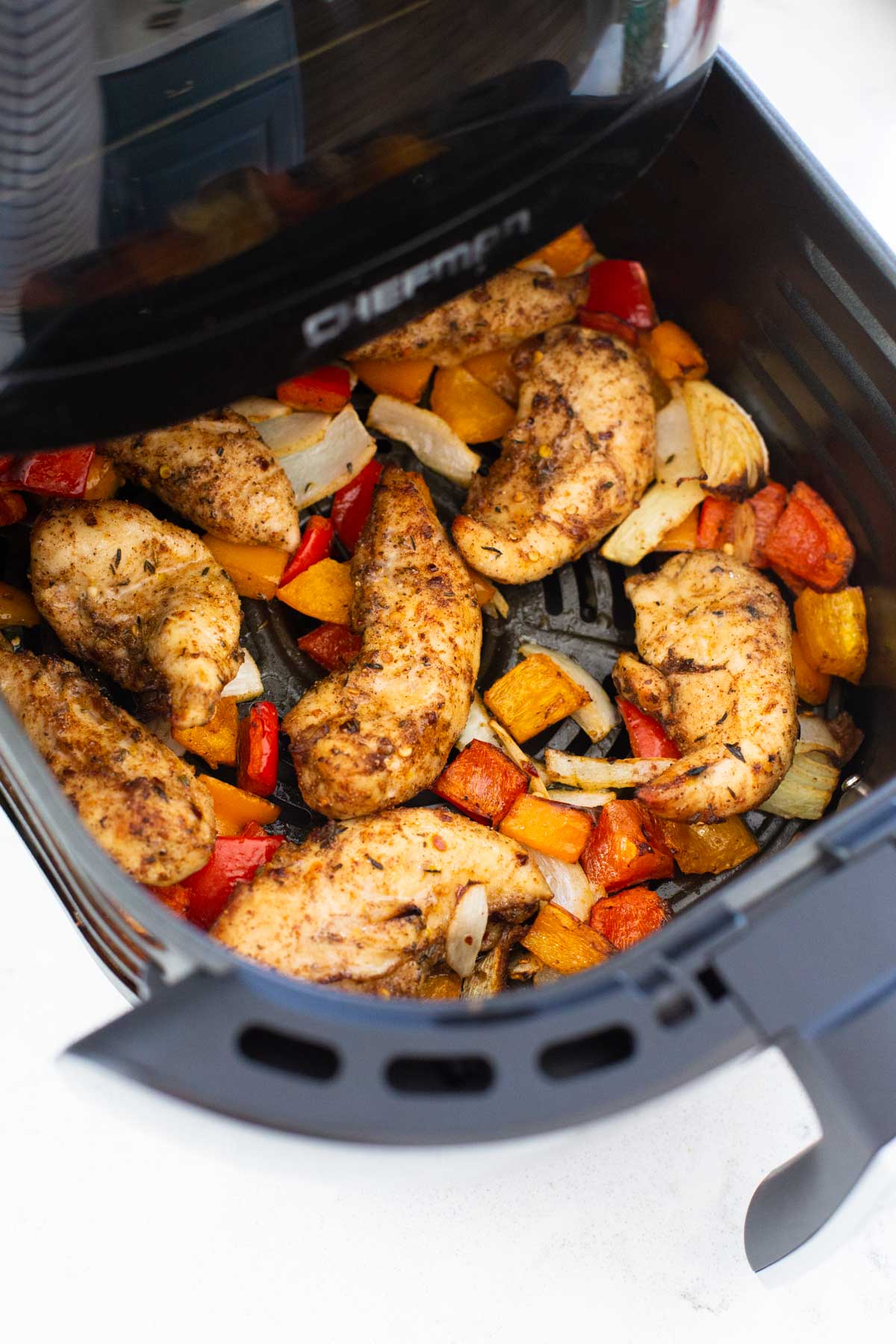 The air fryer basket has been pulled open to show the cooked jerk chicken and peppers.
