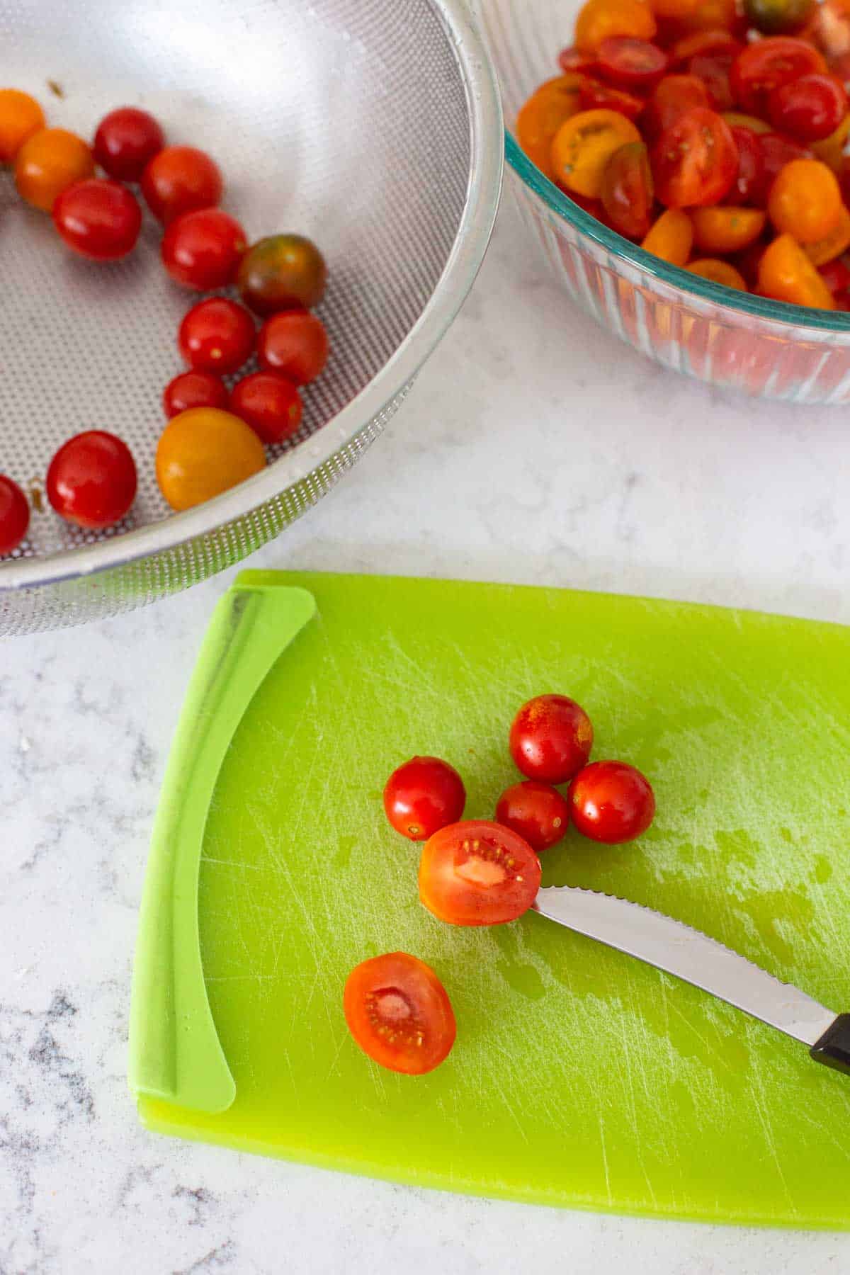 The tomatoes are on a cutting board being cut in half with a serrated paring knife.