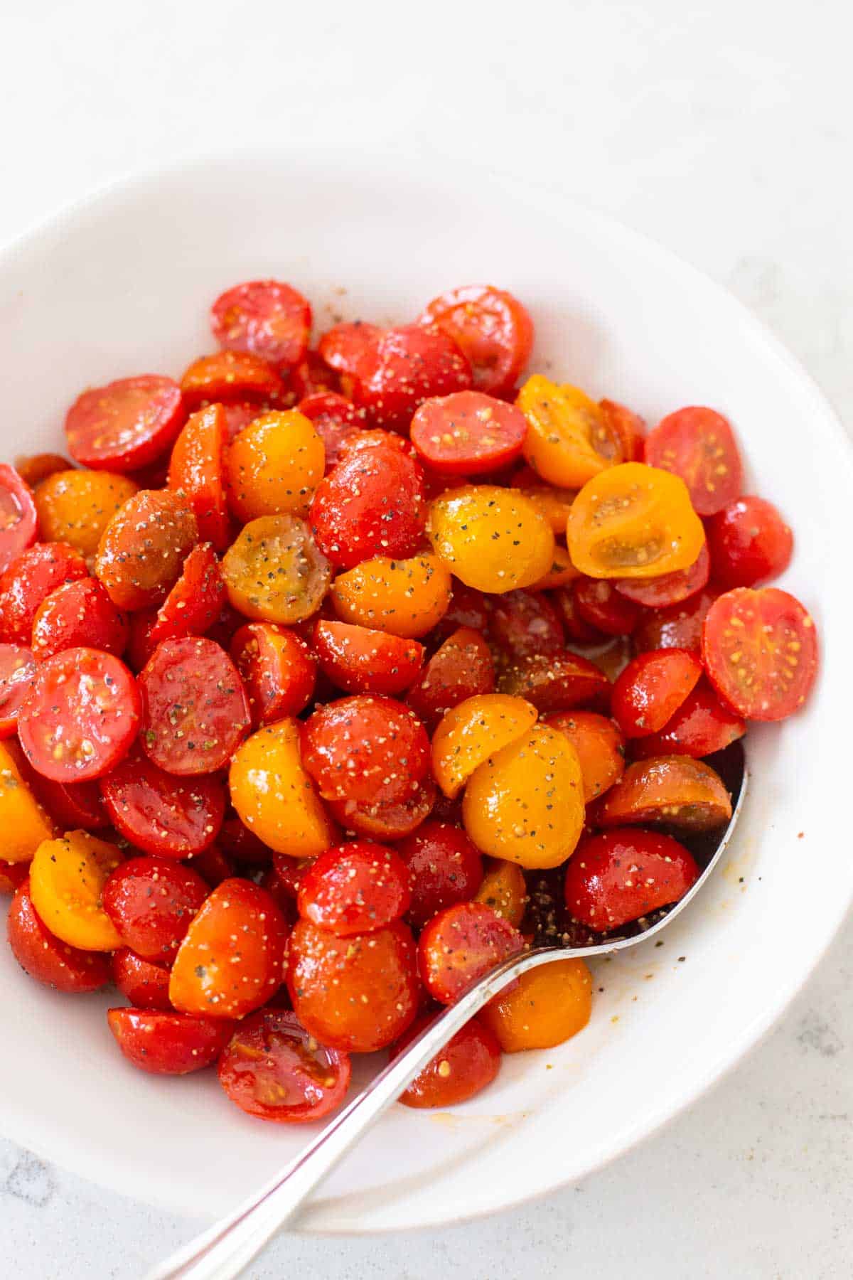 The tomatoes have been marinated and are served in a large white bowl with a spoon.