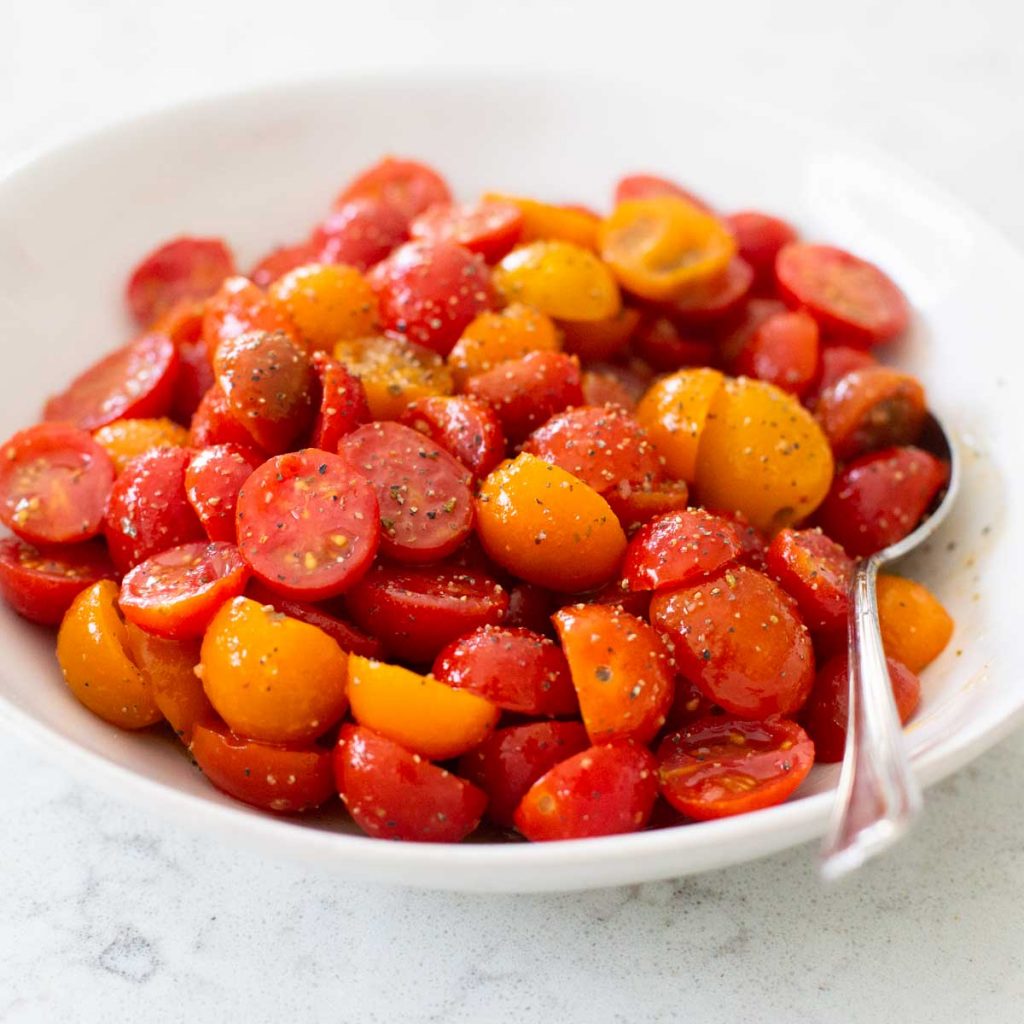 A big bowl of red and yellow cherry tomatoes have been sliced in half and marinated in an Italian dressing.