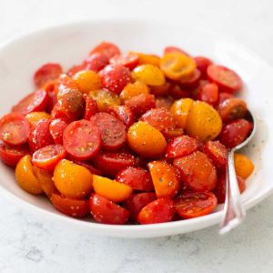 A big bowl of red and yellow cherry tomatoes have been sliced in half and marinated in an Italian dressing.