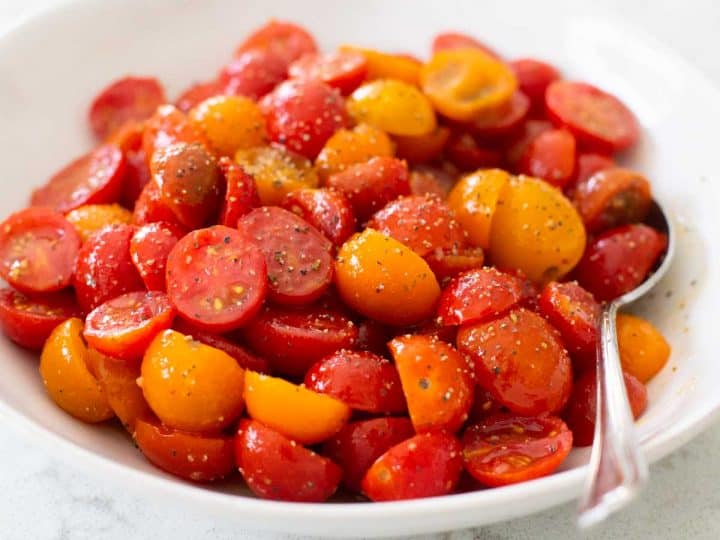 A big bowl of red and yellow cherry tomatoes have been sliced in half and marinated in an Italian dressing.