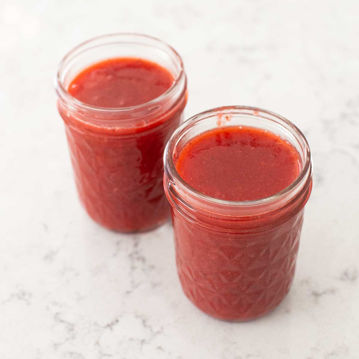 The strawberry sauce has been cooled and ladled into 2 clean mason jars for freezing.