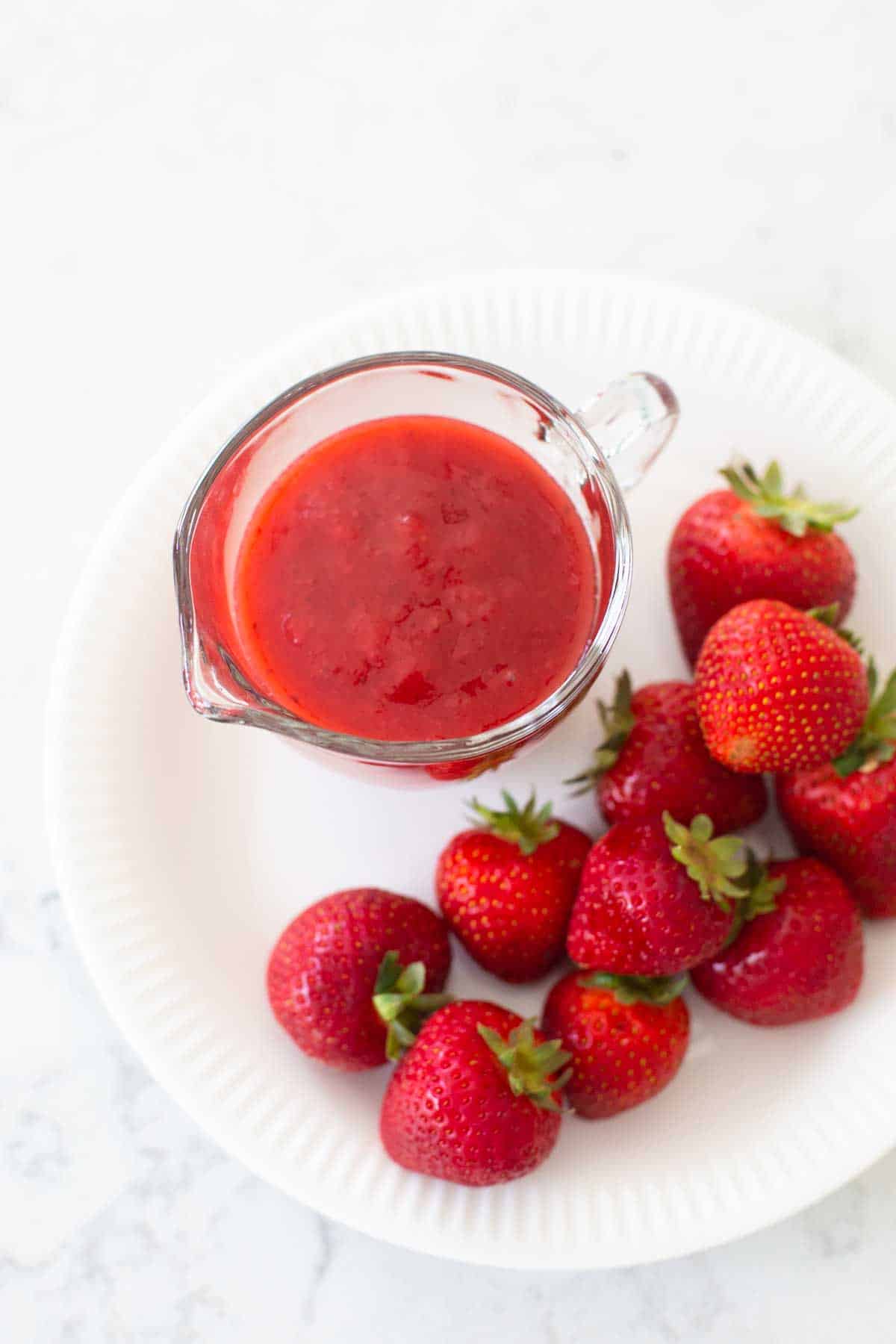 The strawberry sauce is on a plate with fresh berries.