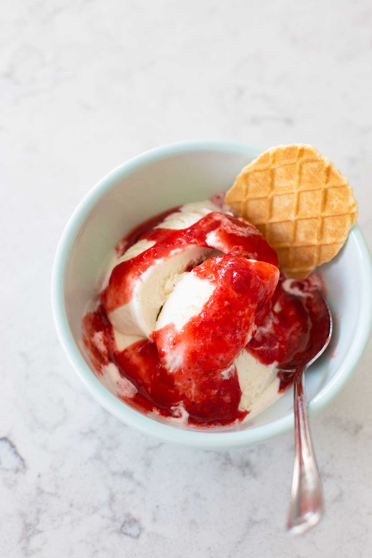 The strawberry sauce has been drizzled over vanilla ice cream and has a waffle cookie.