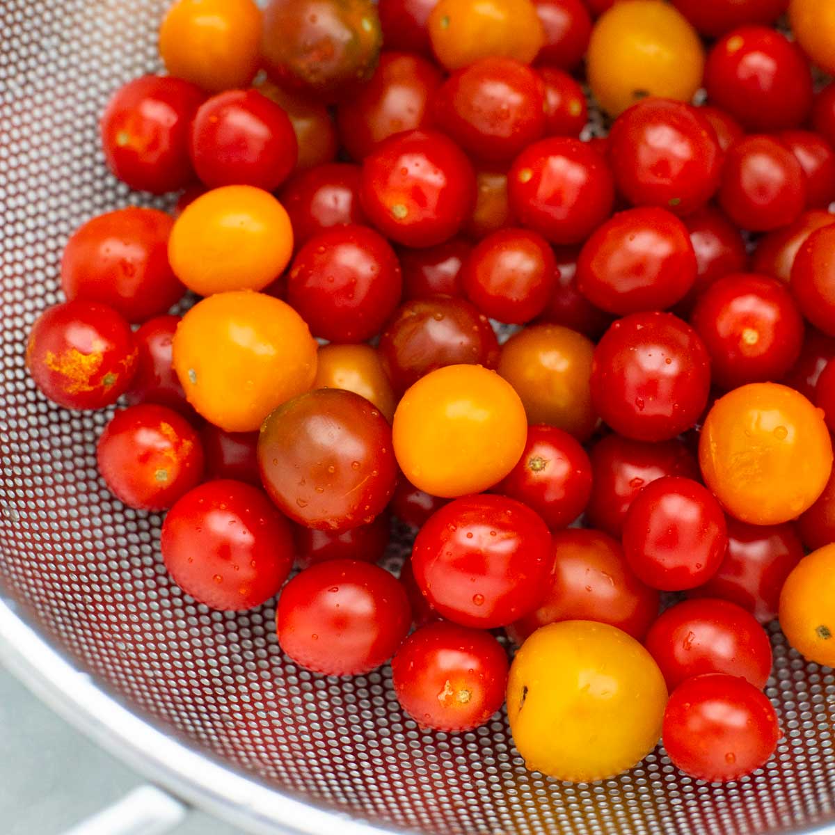 A strainer is filled with raw cherry tomatoes in shades of yellow and red.