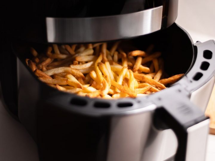 A black air fryer has just finished baking frozen french fries.