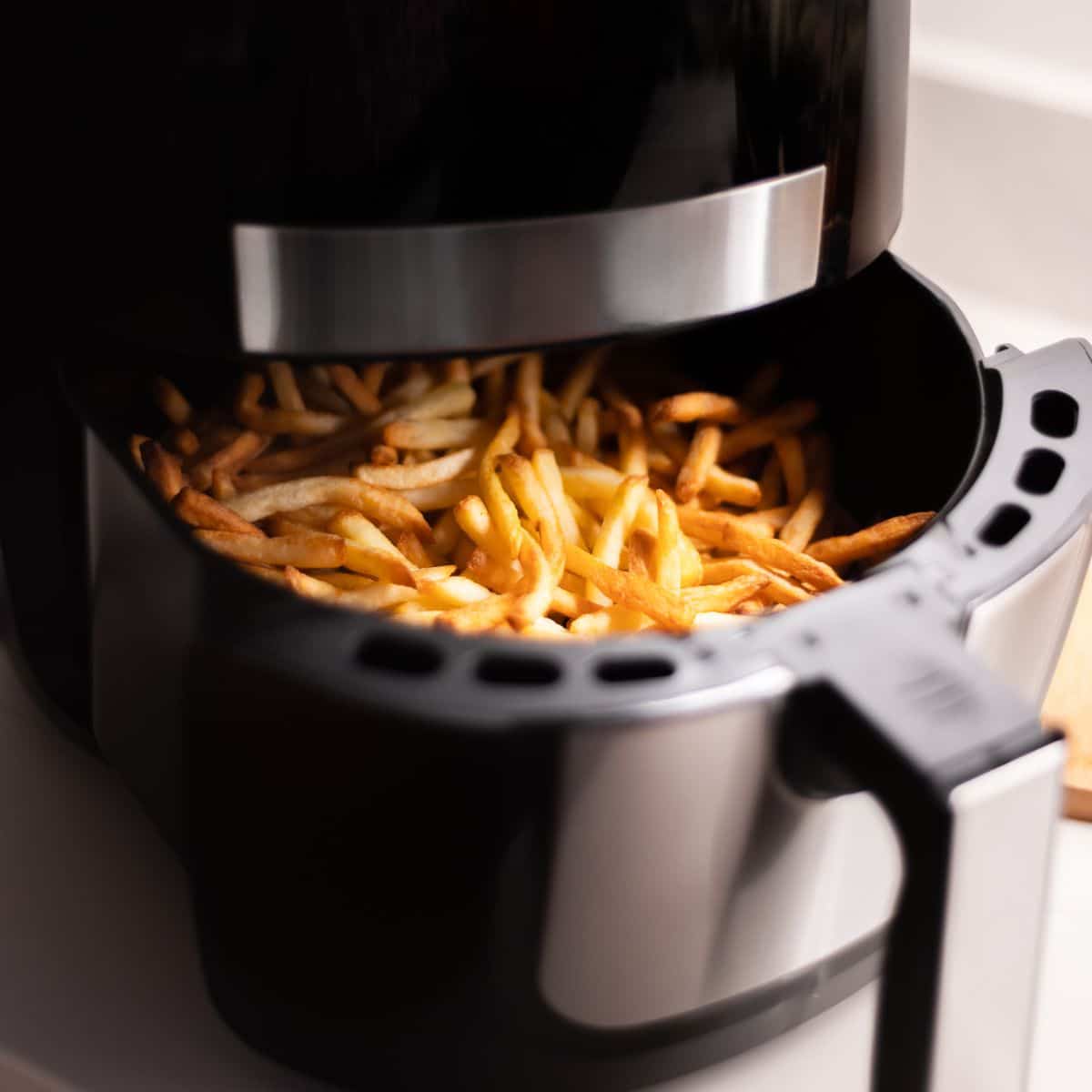 A black air fryer has just finished baking frozen french fries.