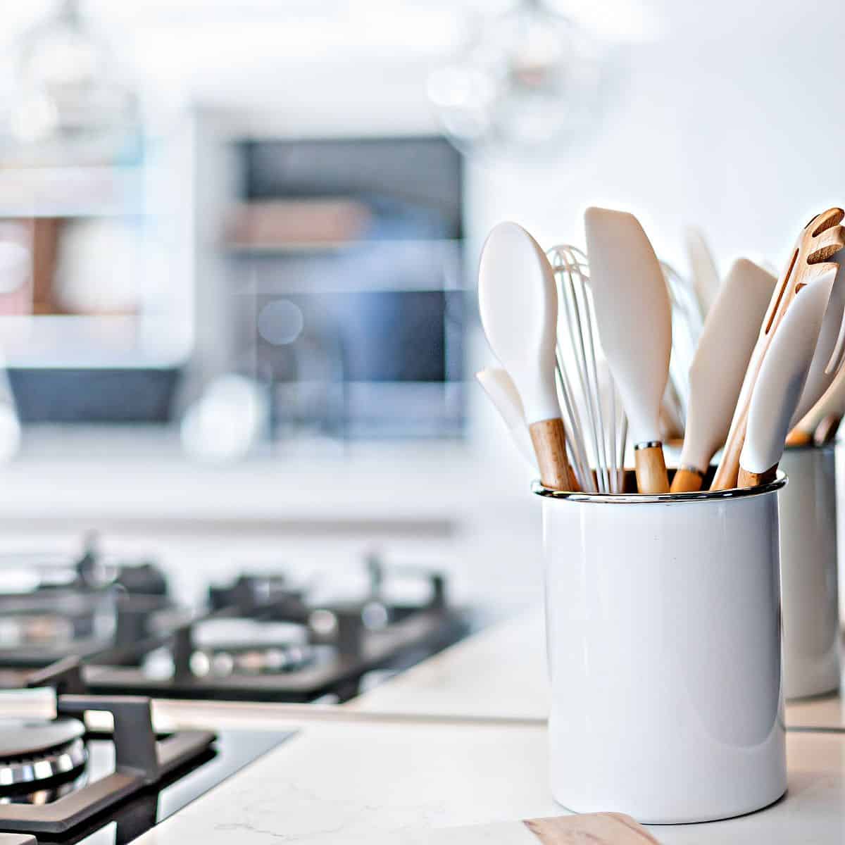 A crock filled with cooking spoons sits next to a gas stove top.