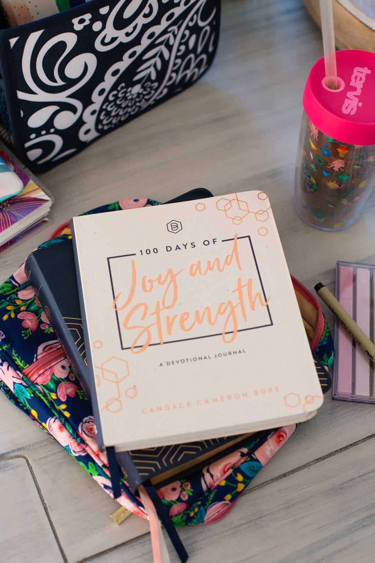 A stack of books features a daily devotional on top of a bible. Iced coffee sitting next to the pile.