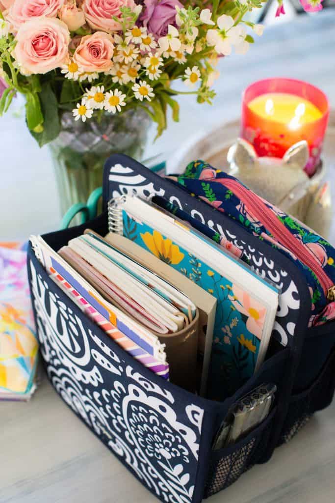 The basket is filled with the journals and planner and is sitting next to fresh flowers and a candle.