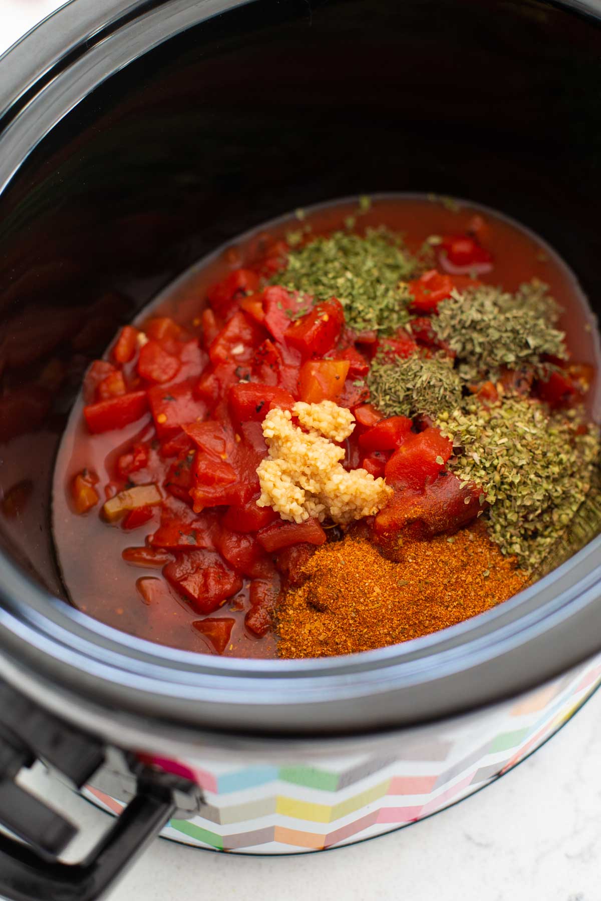 The tomatoes and dried herbs and seasonings are added to the slowcooker.