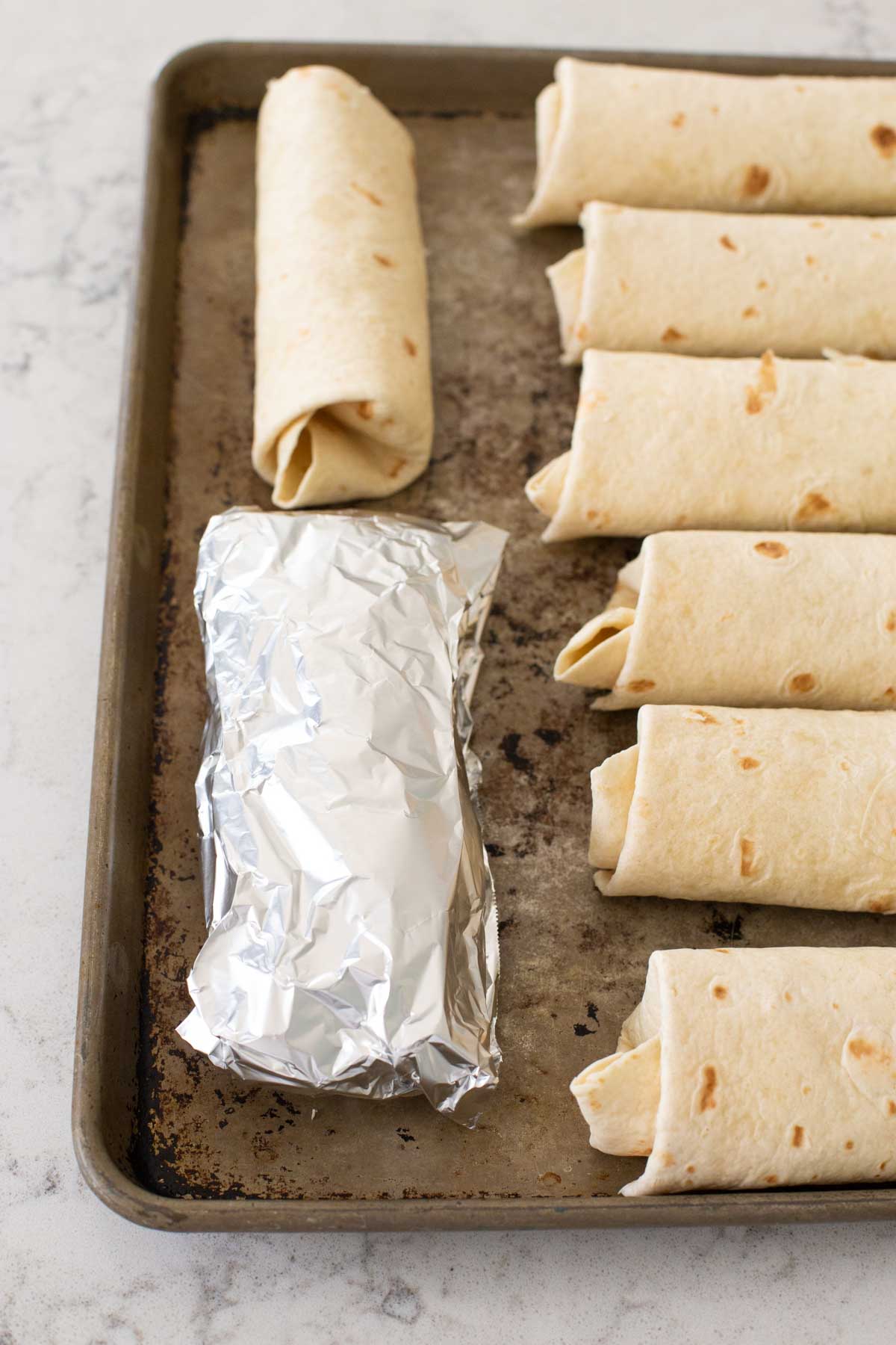 One of the chimichangas is wrapped in aluminum foil for the freezer.