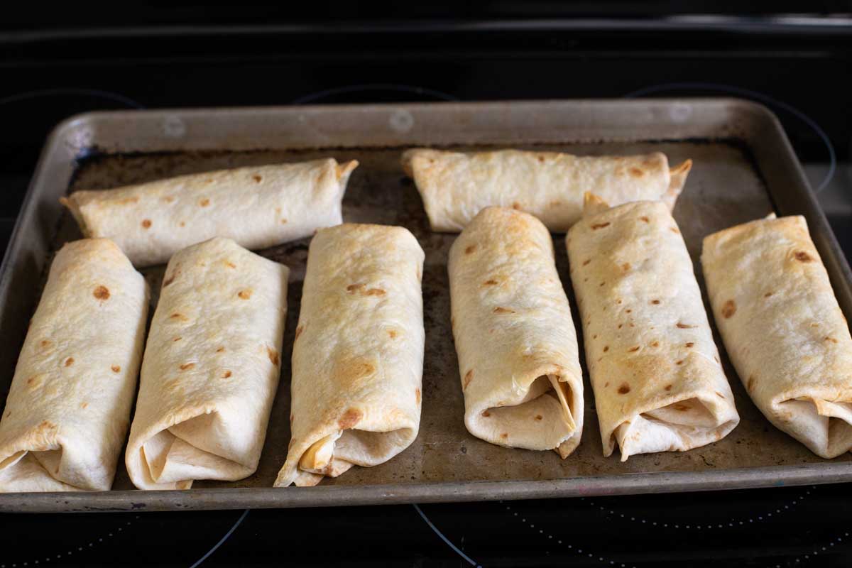 Chimichangas are on a baking sheet.