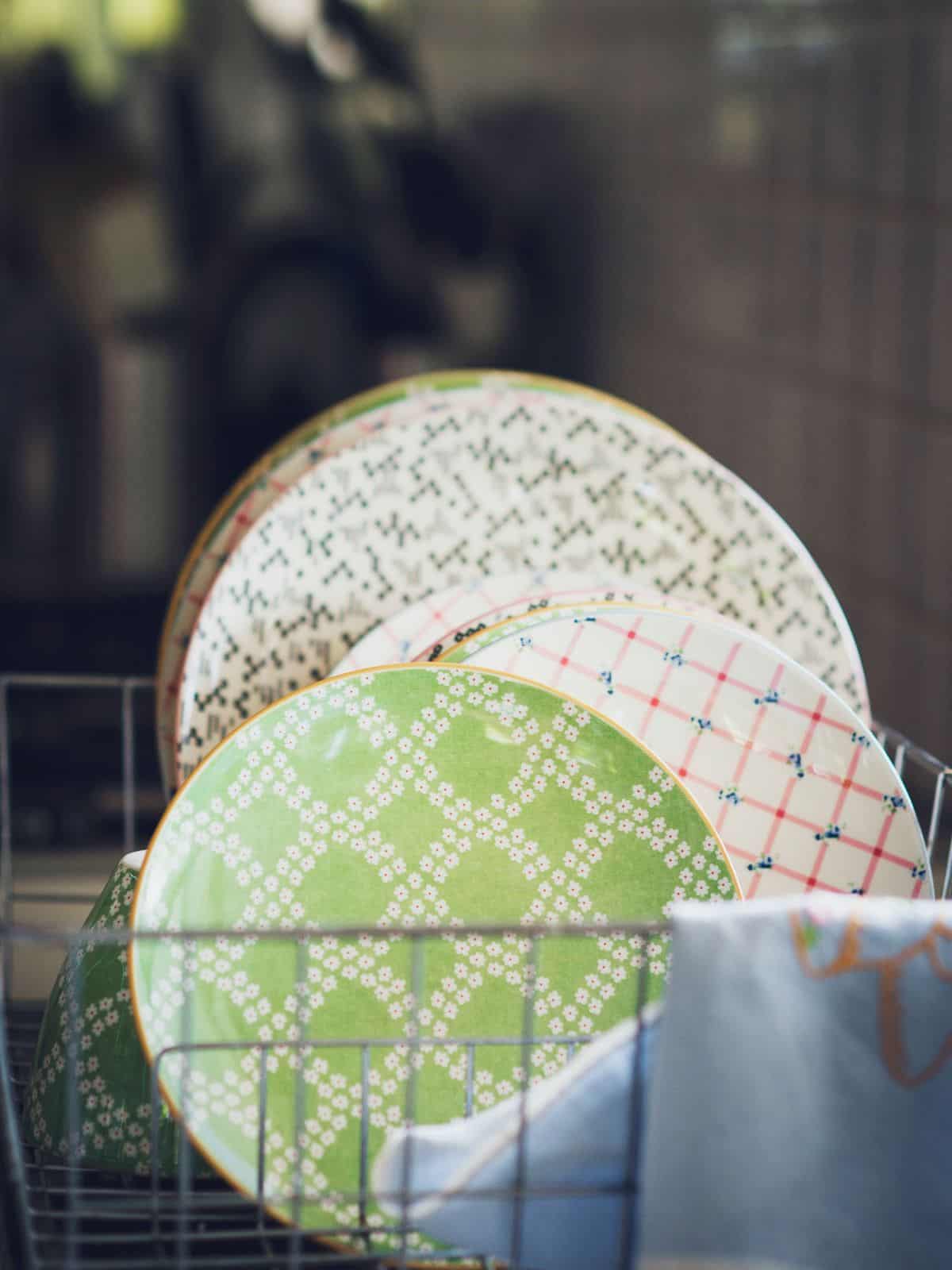 A pile of plates in a drying rack near a sink.