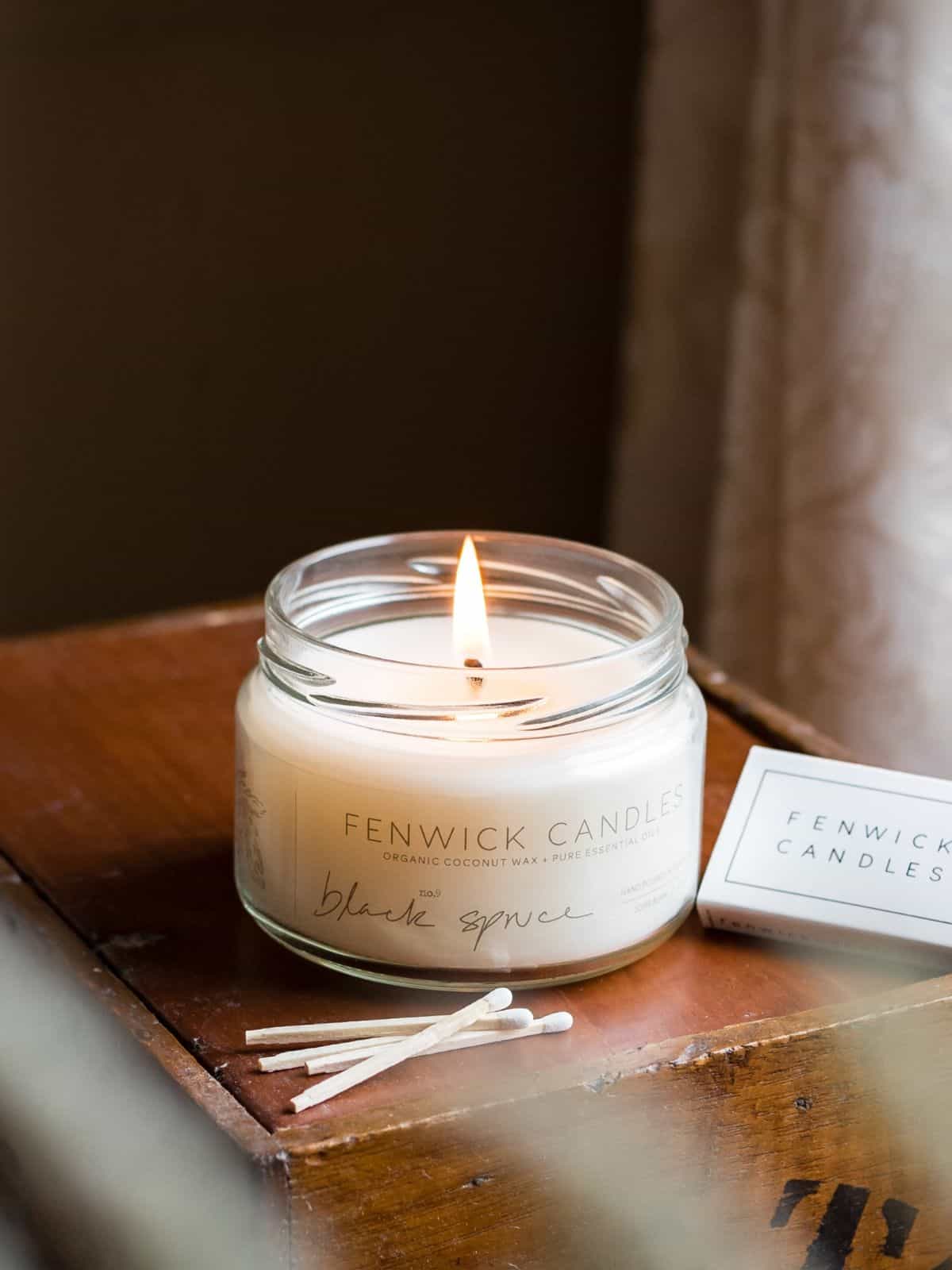 A white jarred candle is lit with matches on the side.