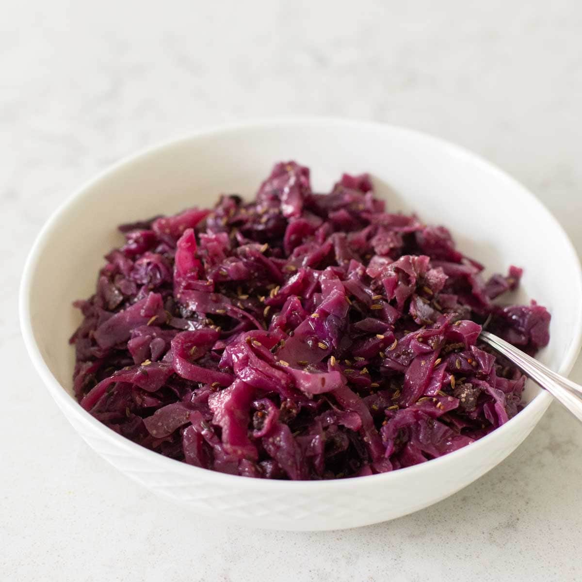 A white bowl filled with shredded cooked red cabbage. 