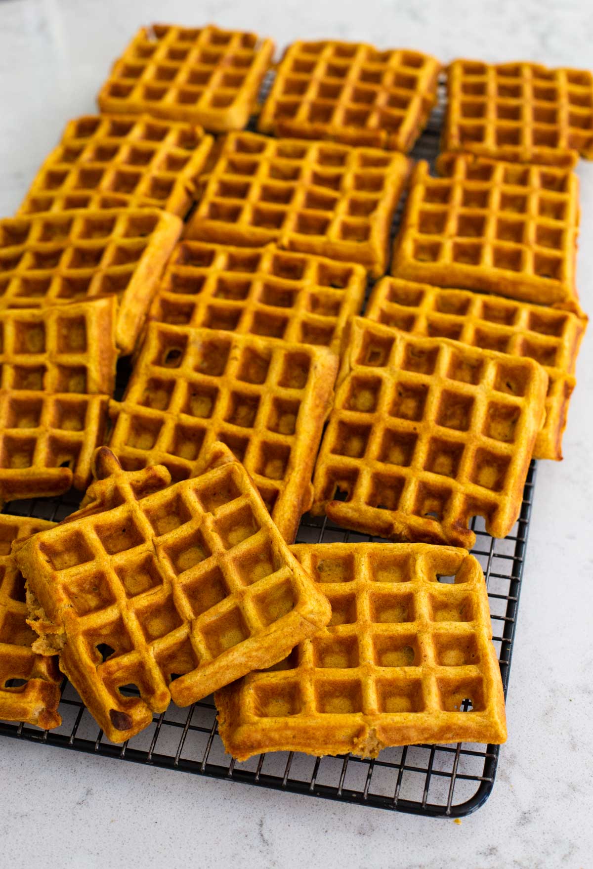 A big batch of pumpkin waffles are cooling on a rack.