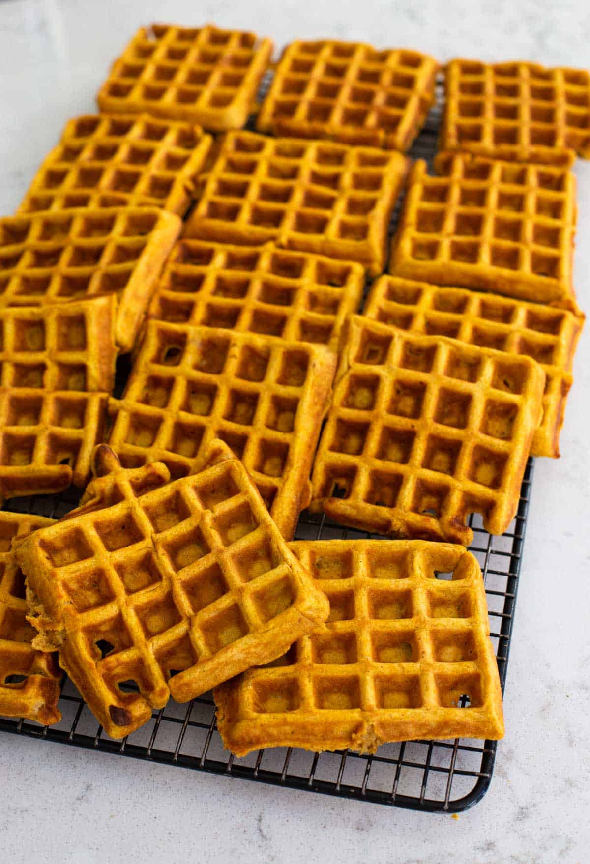 A big batch of pumpkin waffles are cooling on a rack.