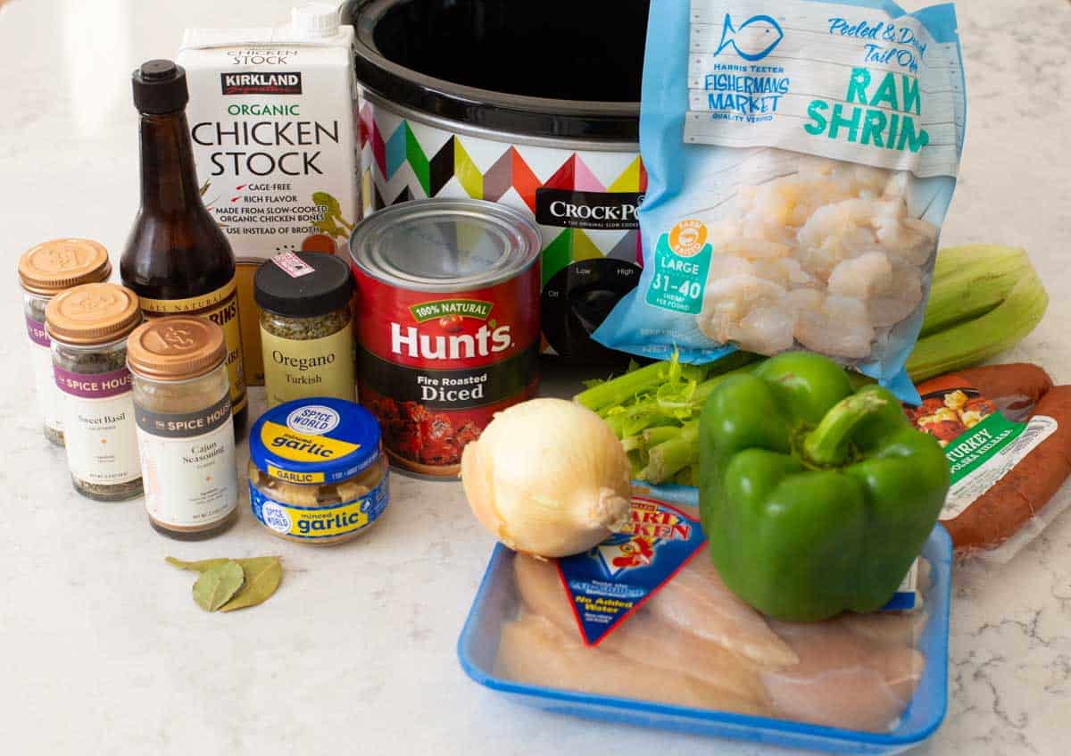 The chicken, shrimp, sausage, and vegetables and seasonings sit in front of a Crockpot.