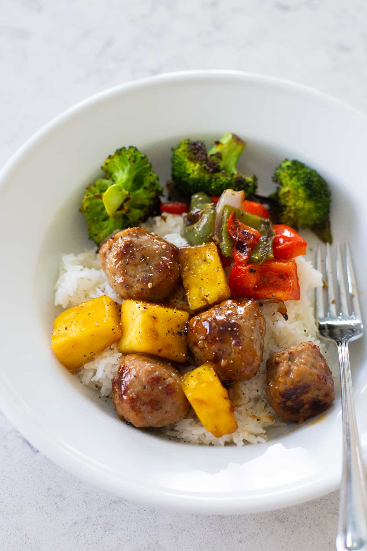 The teriyaki meatballs and pineapple with veggies are spooned over white rice in a bowl.