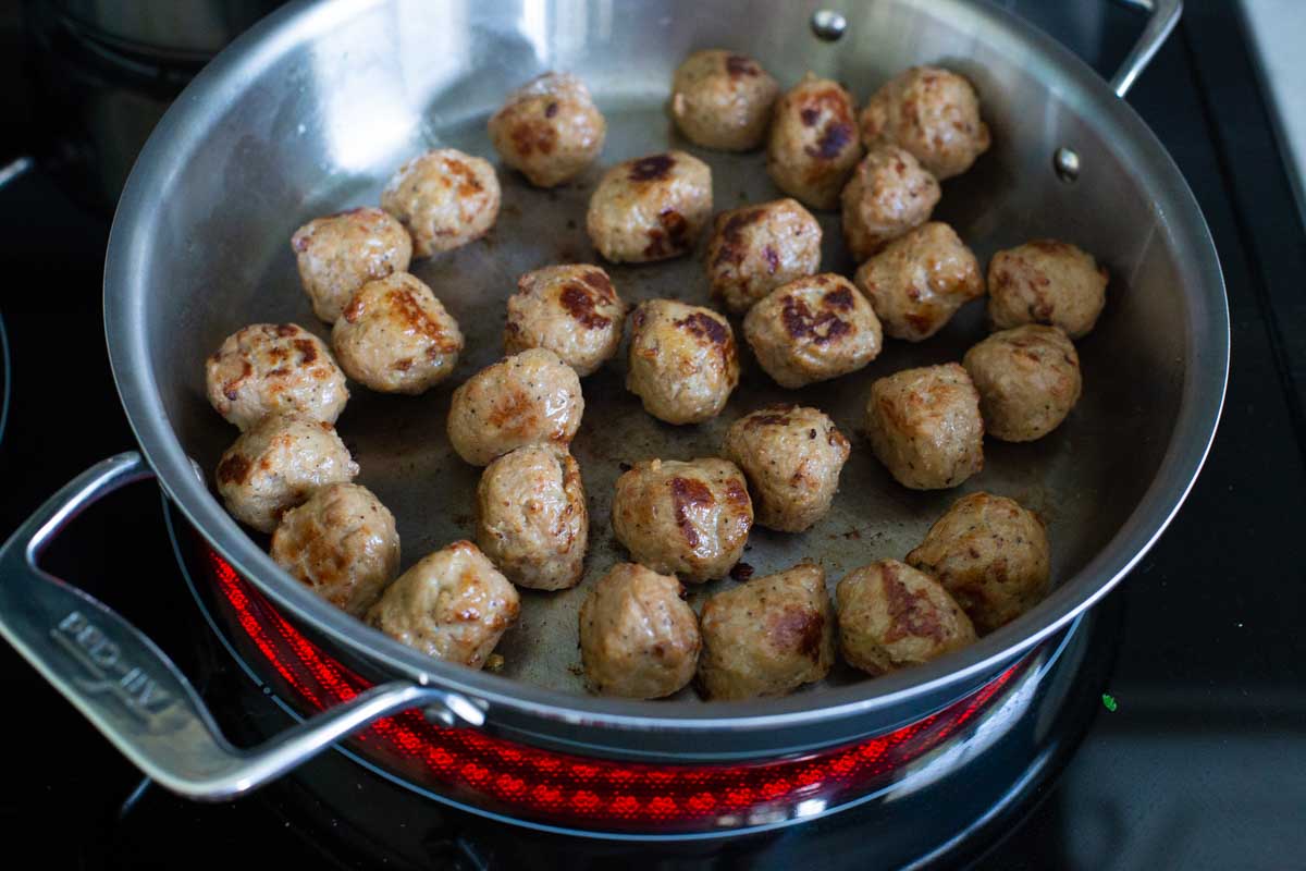 The meatballs are browning in a large skillet.