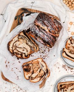 A sliced babka loaf on parchment paper shows the chocolate swirl in each slice.