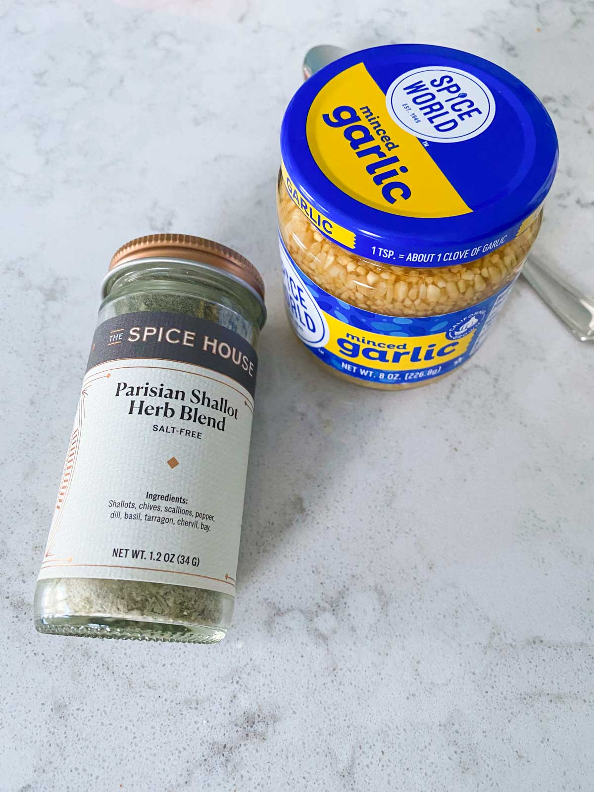 A jar of herbs and a jar of minced garlic on the counter.