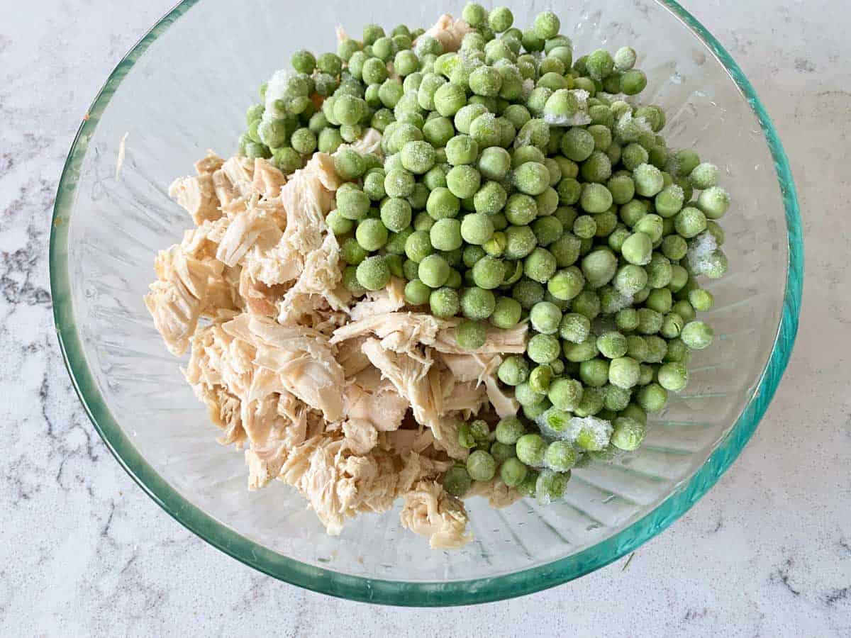 A bowl of shredded chicken with frozen peas waits to be added to the soup.