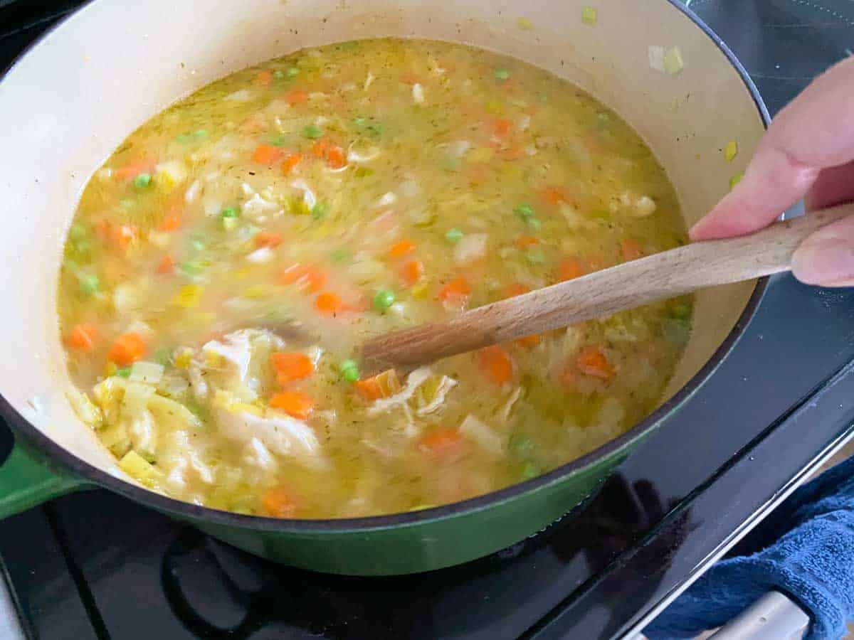 The chicken broth has been added to the soup pot and a spoon is stirring it in.