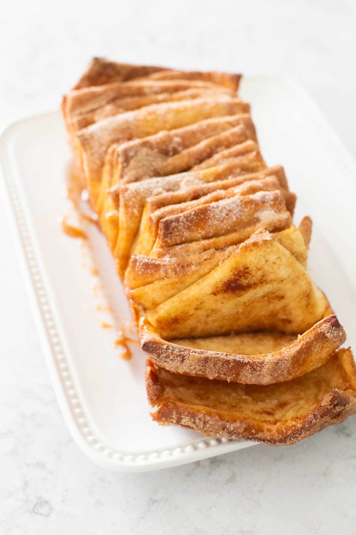 The warm cinnamon pull apart bread has been transferred to a serving platter. A few pieces have been pulled away to show the center of the bread.