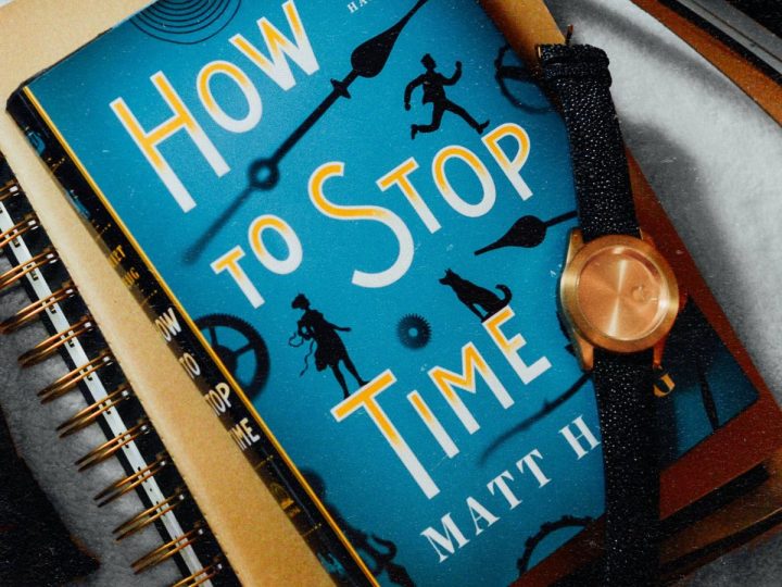 A book called "How to Stop Time" is next to a watch.