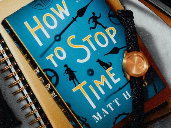 A book called "How to Stop Time" is next to a watch.