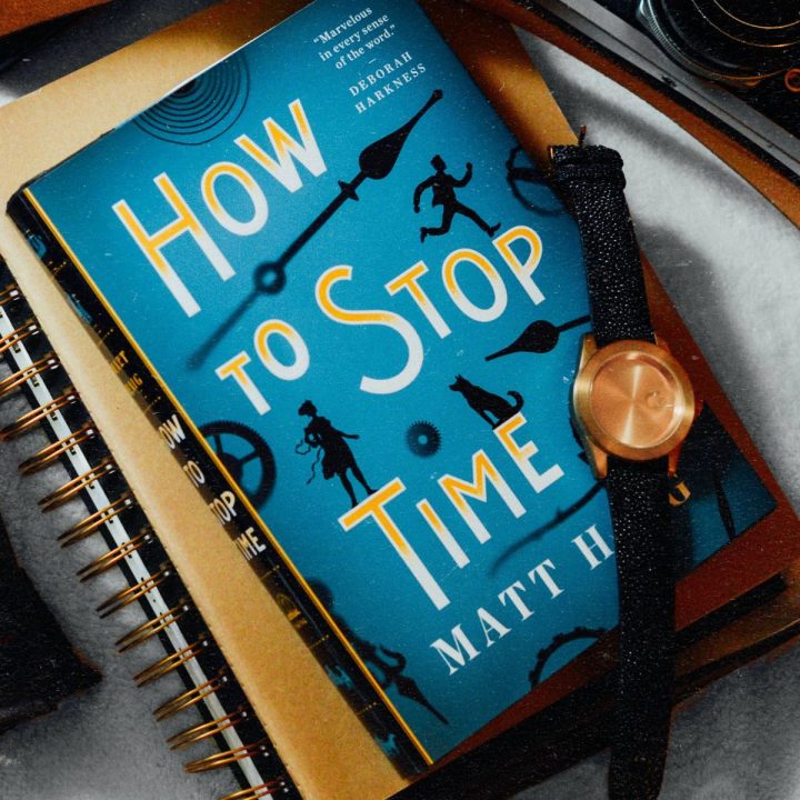 A book called "How to Stop Time" is next to a watch.