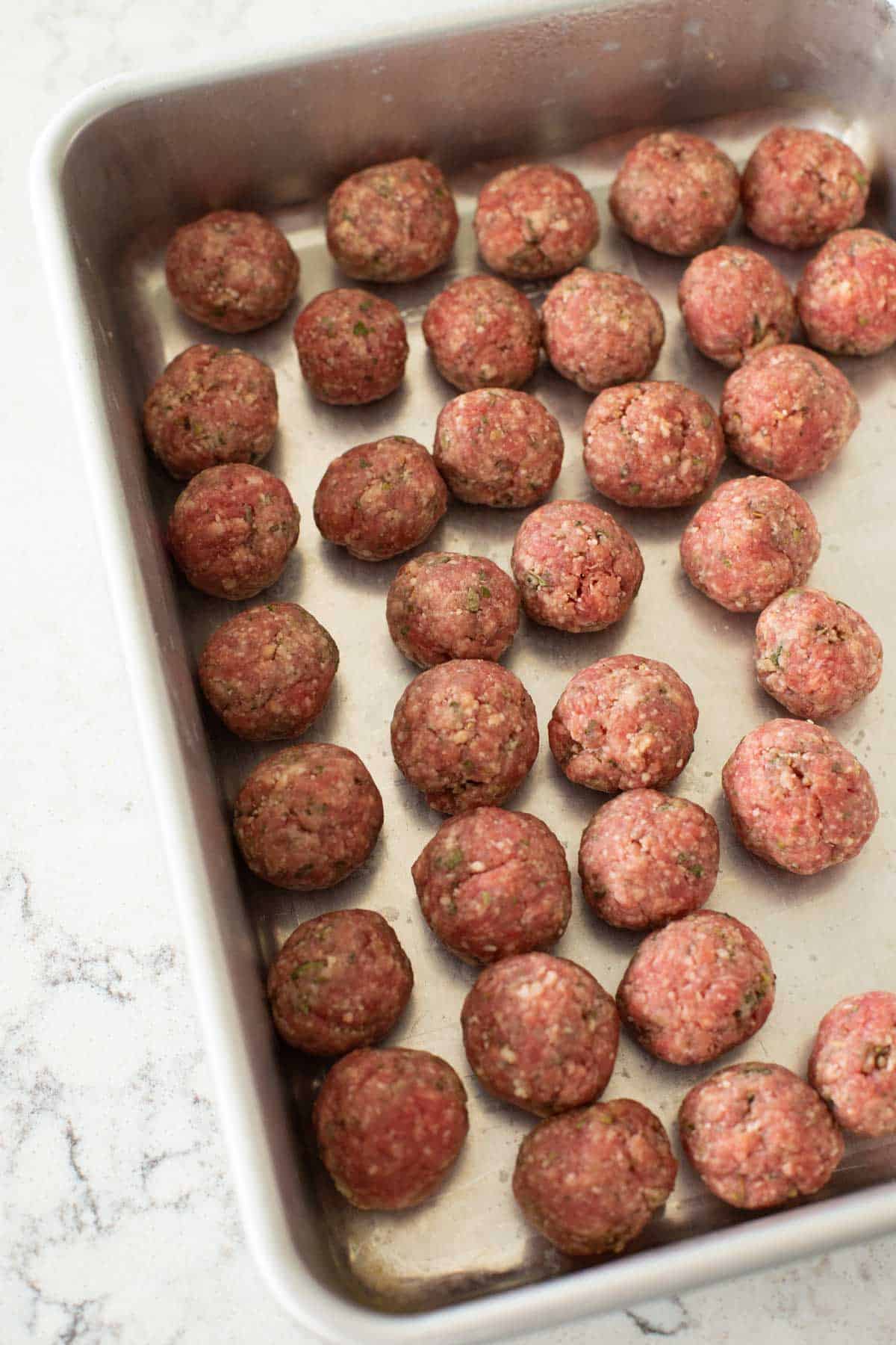 The rolled Italian meatballs are lined up in a baking pan for storage.